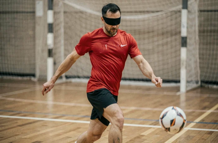 Joueur de cécifoot portant un masque occultant effectuant un tir sur un terrain sportif intérieur