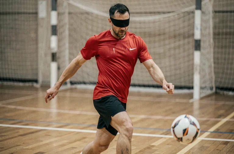 Joueur de cécifoot portant un masque occultant effectuant un tir sur un terrain sportif intérieur